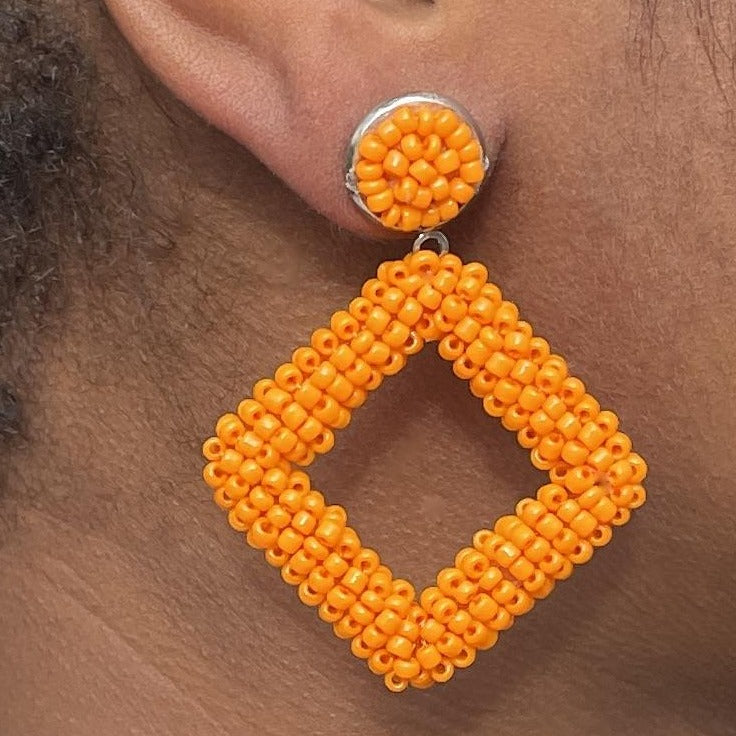 Right ear of a person wearing an orange beaded dangle earring with large stud and square pendant