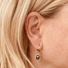 Right ear of a person wearing a small golden huggie hoop earring with flamingo design pendant