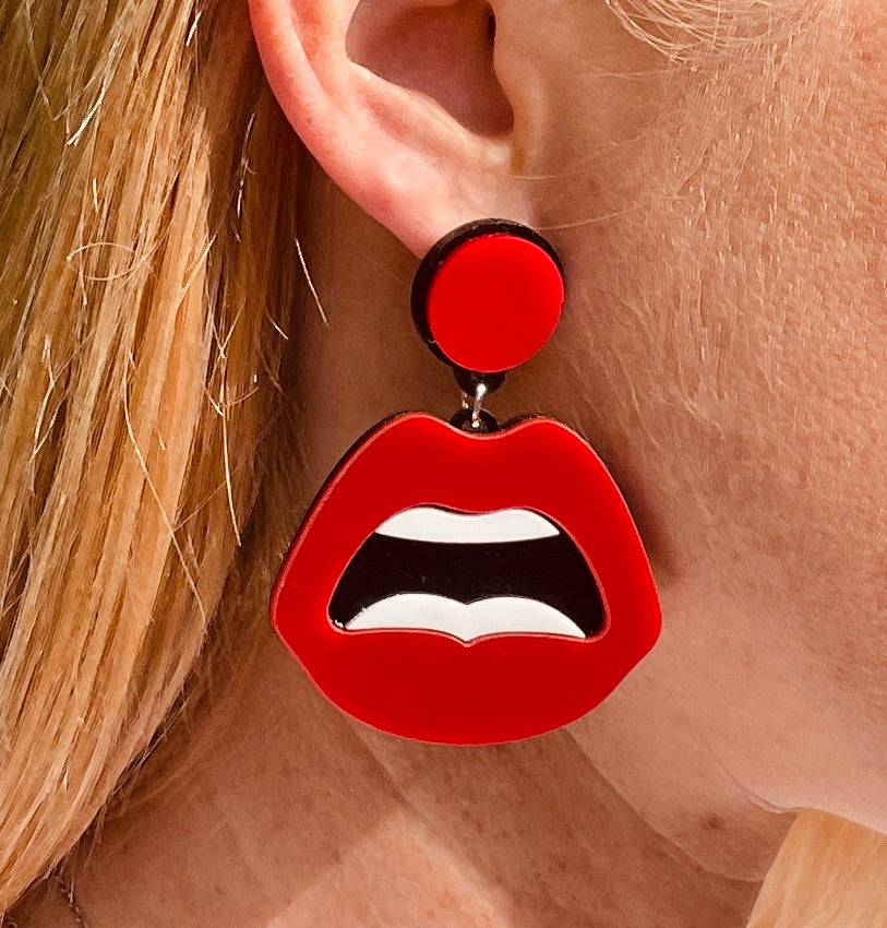 Right ear of a person wearing an acrylic statement earring with red circular stud and large lip-shaped pendant