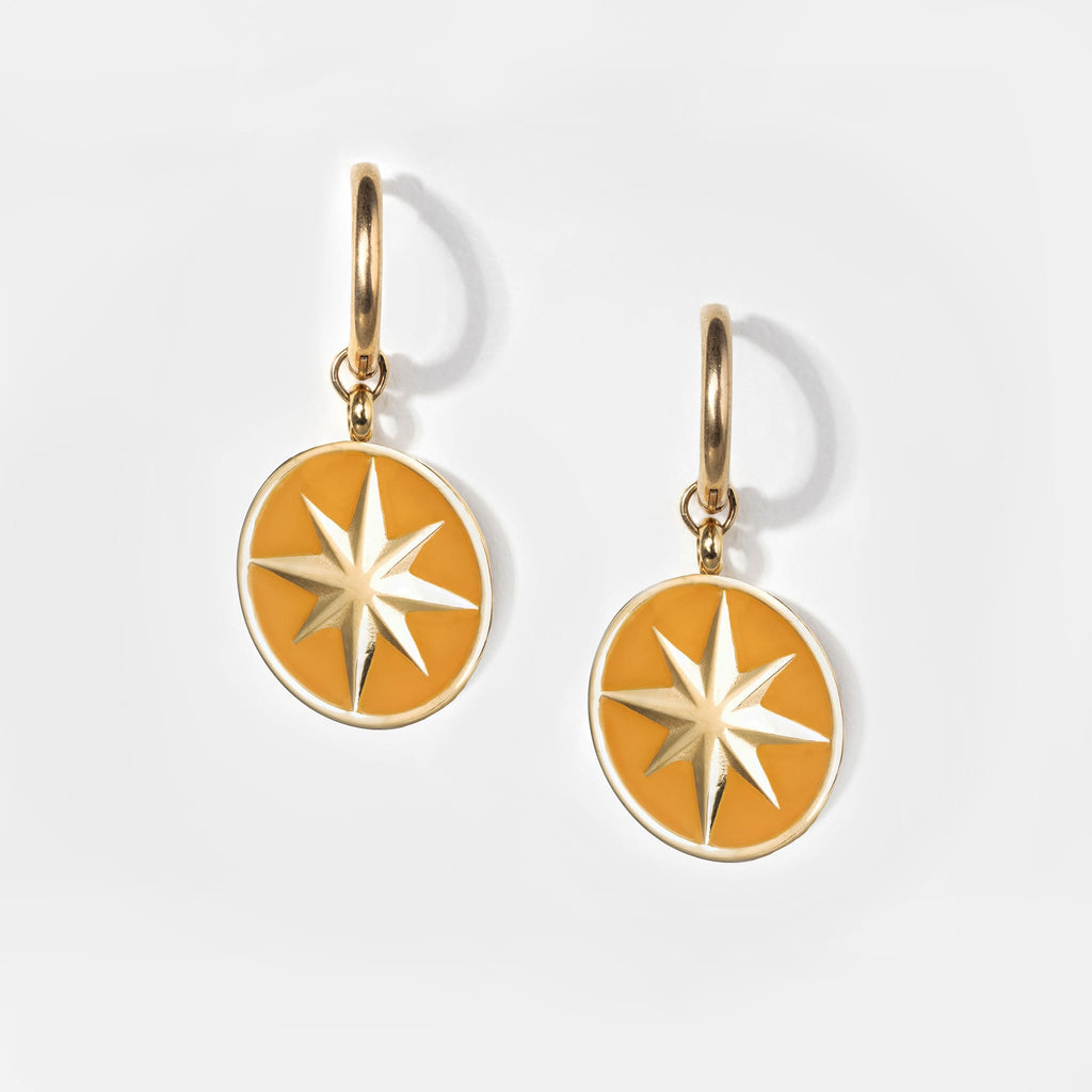 Pair of small golden huggie hoop earrings with a round pendant in golden yellow and a gold star