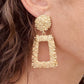 Right ear of a person wearing a statement earring in textured gold effect with a large round stud and rectangular pendant
