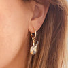 Left ear of a person wearing a small, golden peace hand drop earring in multicolour zircon design