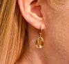 Right ear of a person wearing a small gold pierced hoop huggie earring with shell pendant