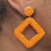 Right ear of a person wearing an orange beaded dangle earring with large stud and square pendant  