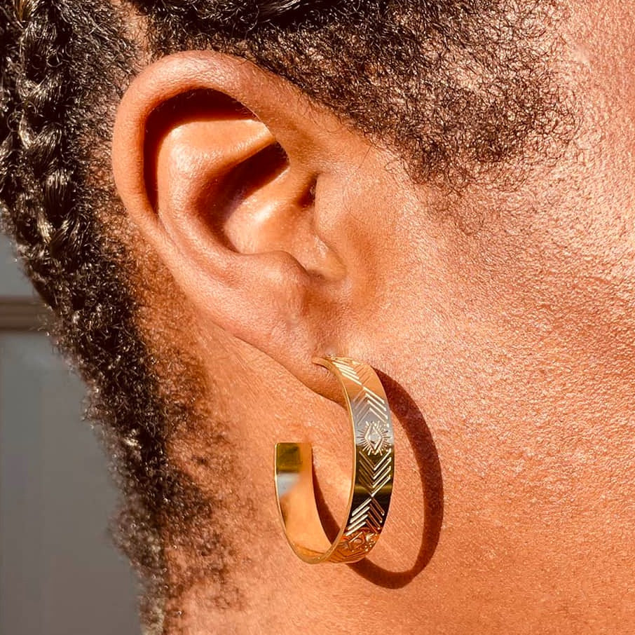Right ear of a person wearing a gold hoop pierced earring with aztec pattern