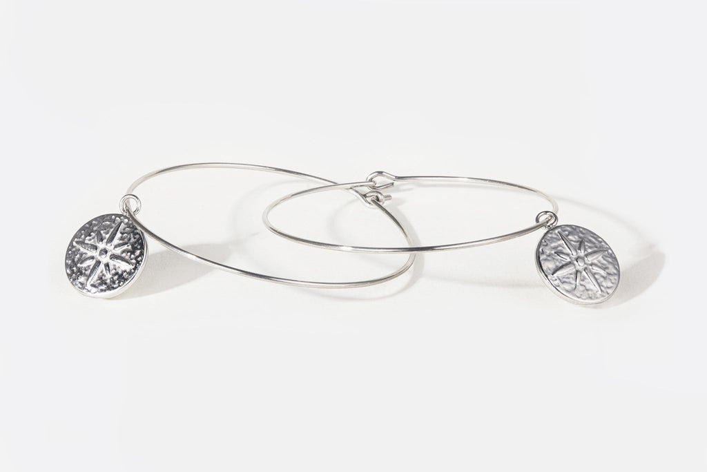 Pair of large, thin silver hoop earrings with round embossed pendant with star detail
