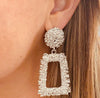 Left ear of a person wearing a statement pierced earring in textured silver effect with a large round stud and rectangular pendant