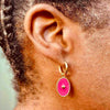 Right ear of a person wearing a small gold pierced hoop huggie earring with hot pink pendant