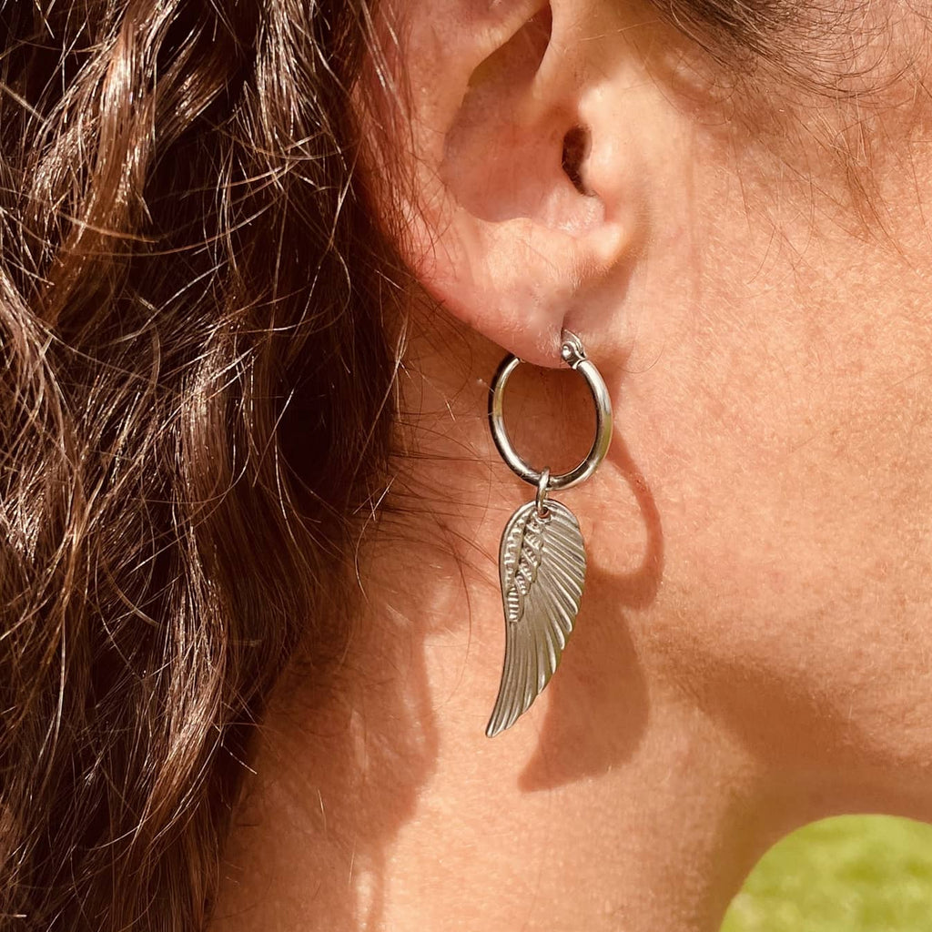 Right ear of a person wearing a silver earing with a hoop and drop pendant in the shape of a silver wing