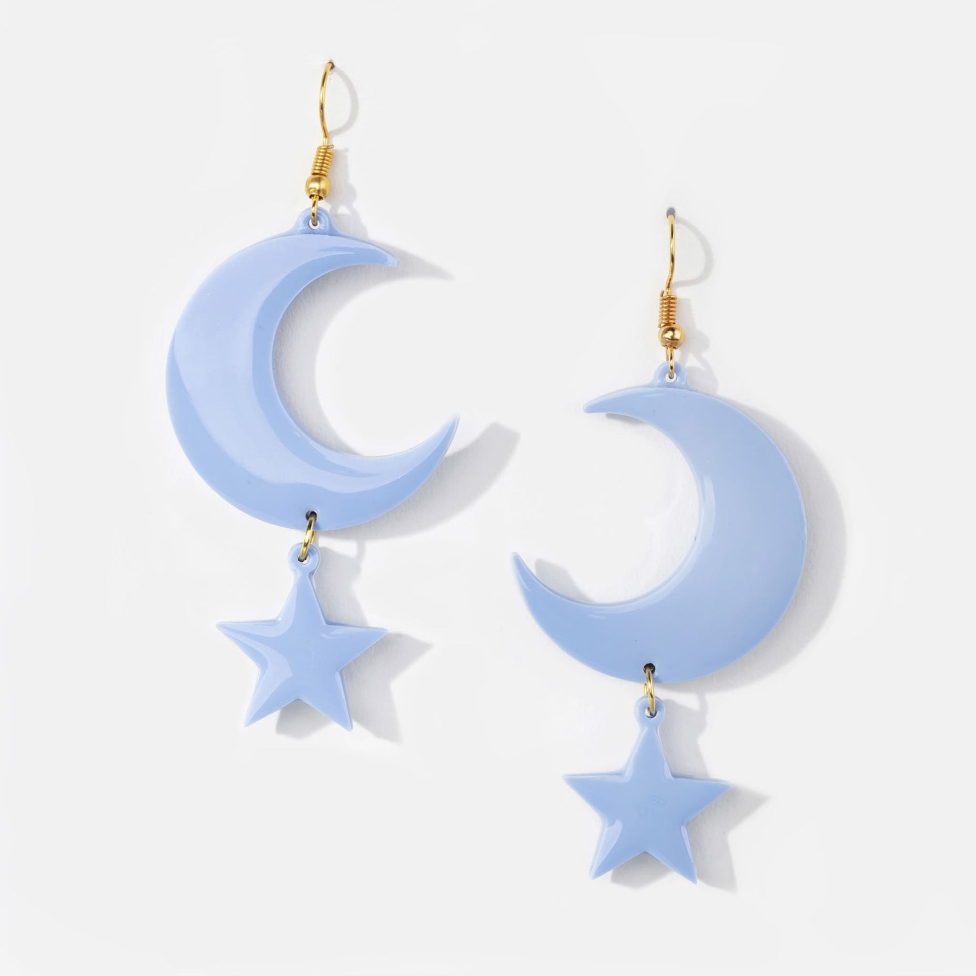 Pair of pale blue resin statement pierced earrings with gold hook clasp and moon and star shaped pendant design